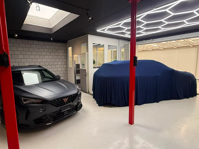 Cupra Formentor in Mattgrau und abgedecktes Fahrzeug unter der Wabenbeleuchtung im Showroom